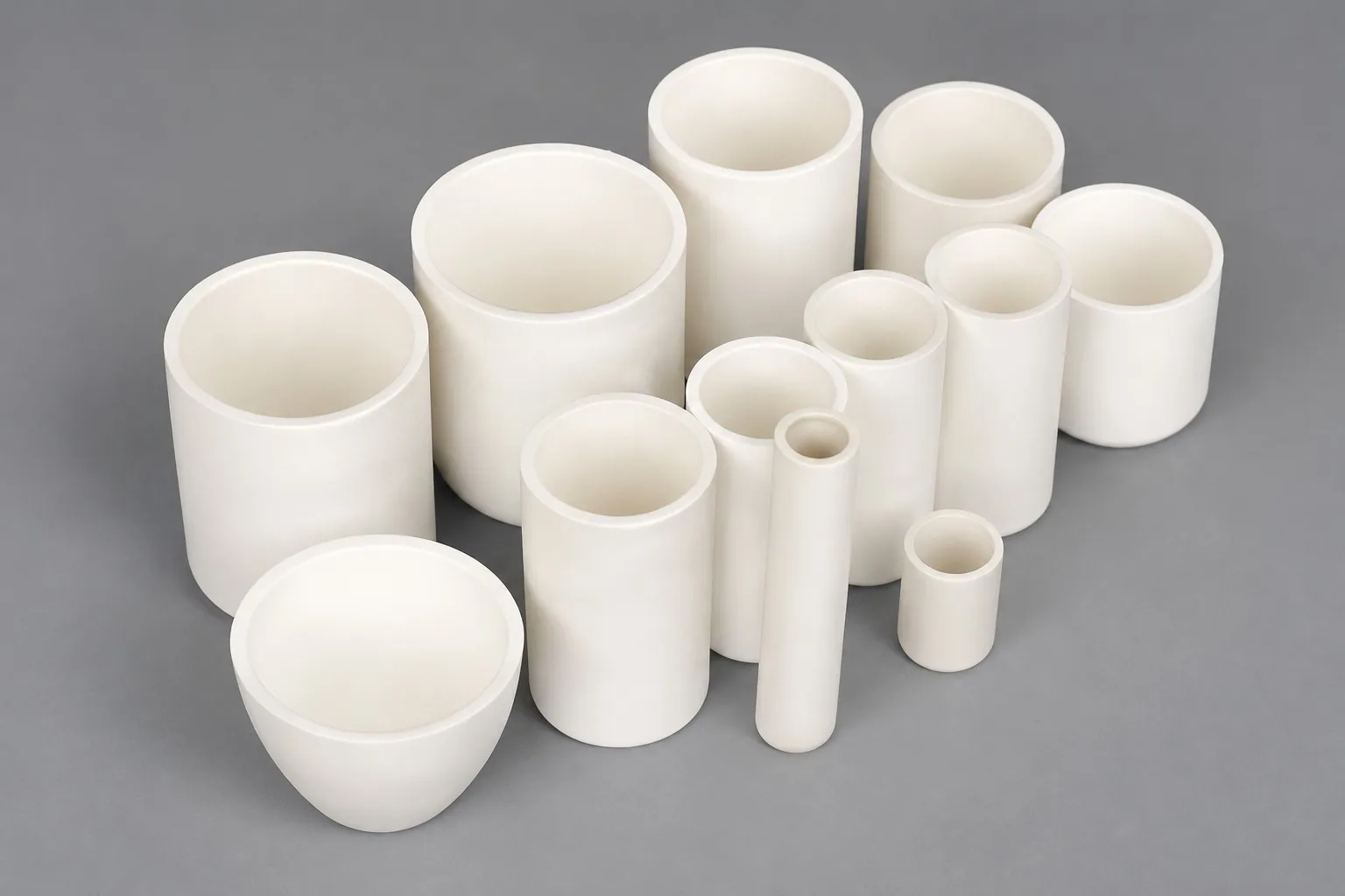 About a dozen white alumina crucibles of different diameters and depths on a grey studio ground.
