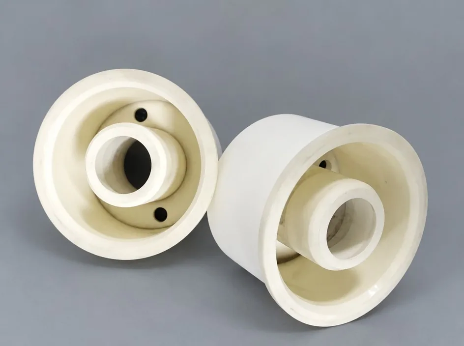 Two white alumina cup-shaped bodies on a grey studio ground, each with an internal central boss and two small holes in the rim.