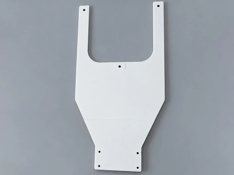 A flat white alumina fork plate with a rounded yoke and drilled holes at both tips, on a grey studio ground.