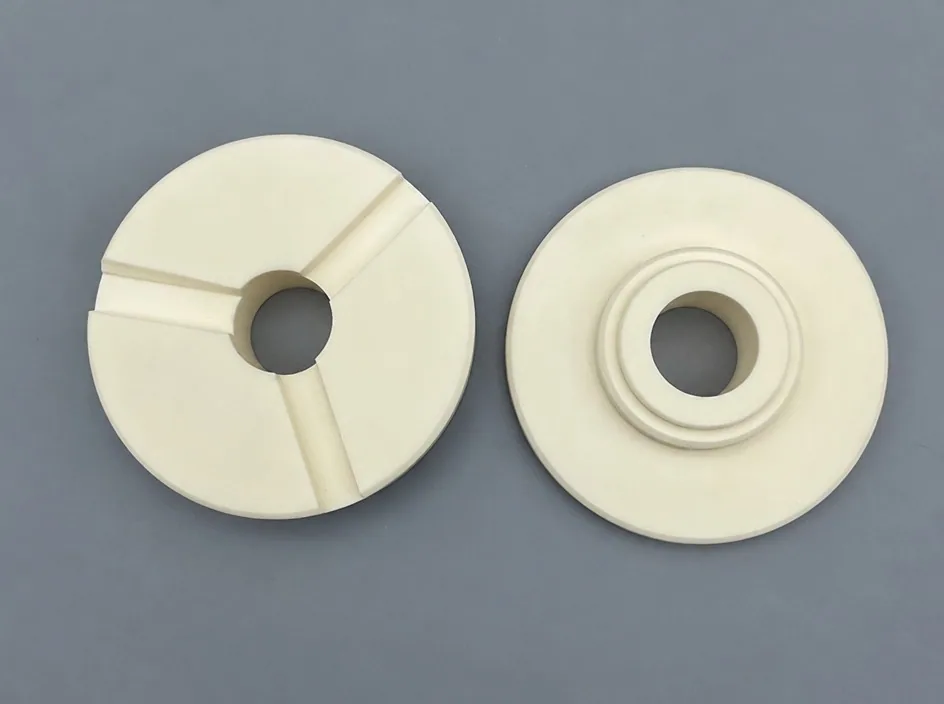 Two white alumina discs on a grey studio ground: one face carries three radial slots, the other a stepped boss around the bore.