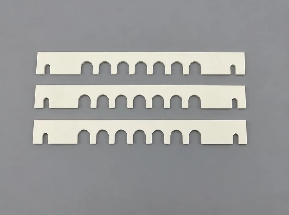 Three long white alumina bars on a grey studio ground, each with a row of U-shaped notches cut along one edge.