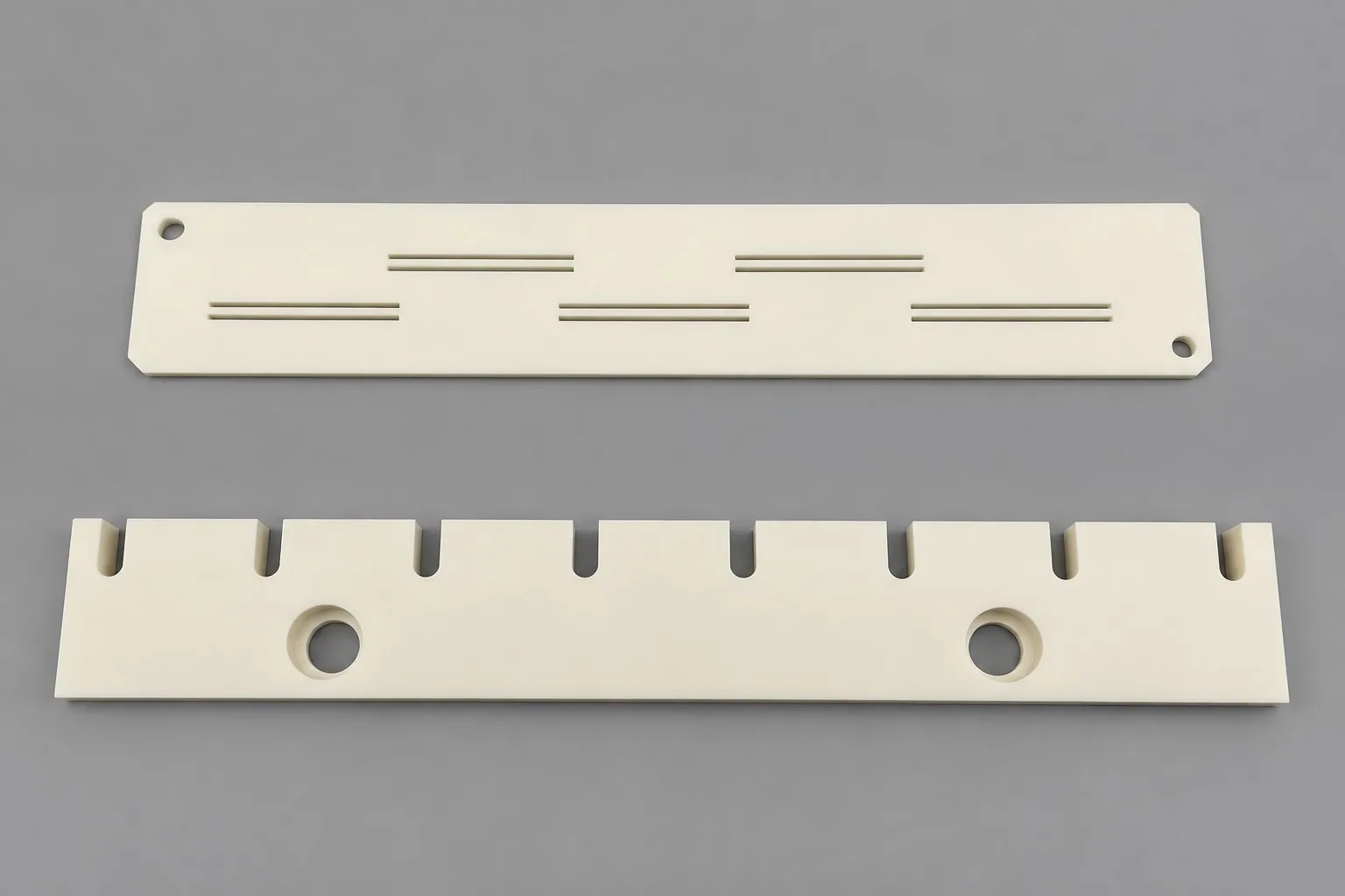 Two rectangular white alumina plates: one carries milled slots on its face, the other edge slots and two large bores.