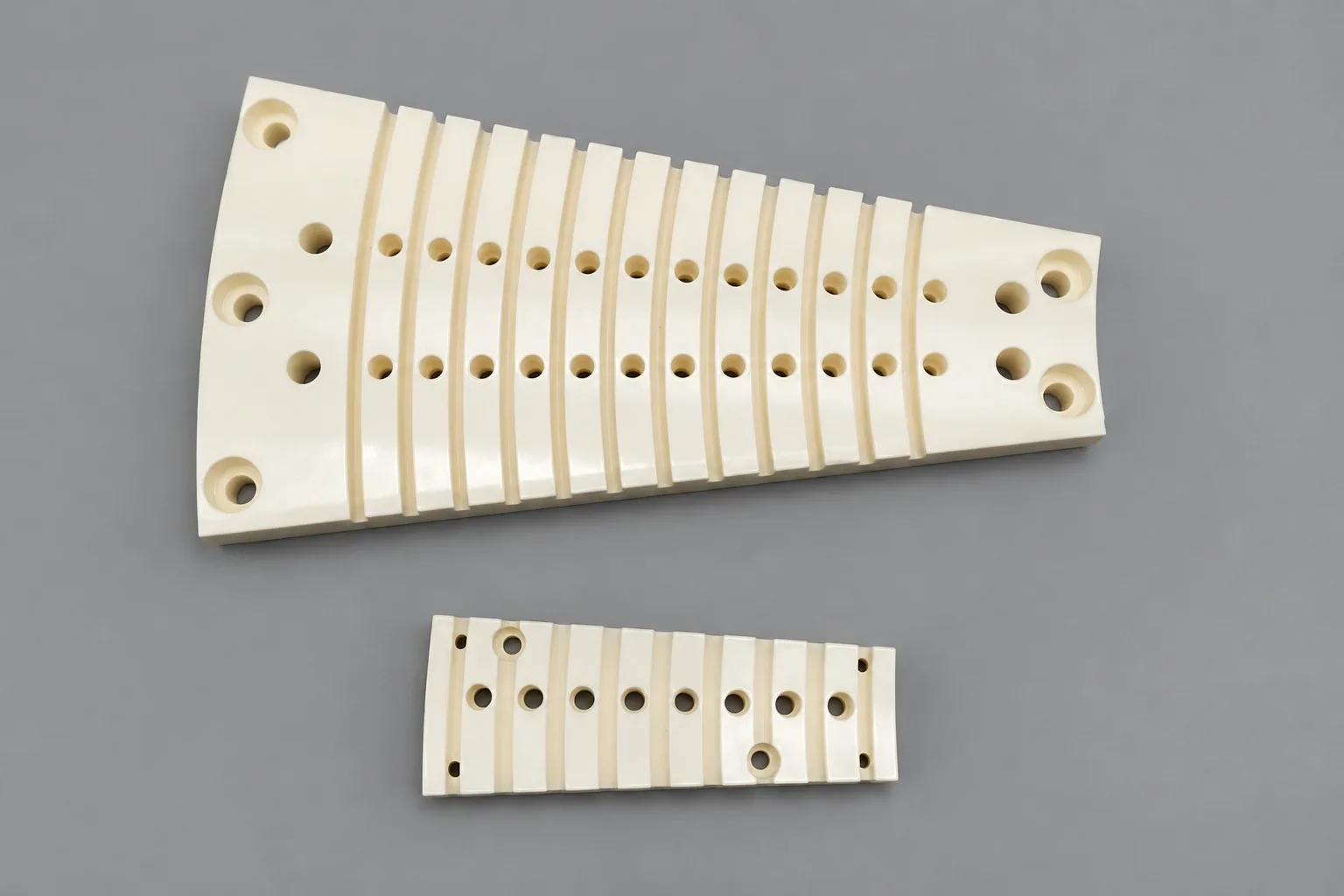 Two tapered white alumina plates pierced by rows of small holes and radial slots, on a grey studio ground.