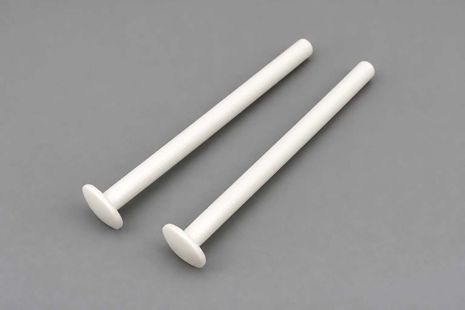 Two white alumina pins on a grey studio ground, each with a long shaft and a flat flanged head.