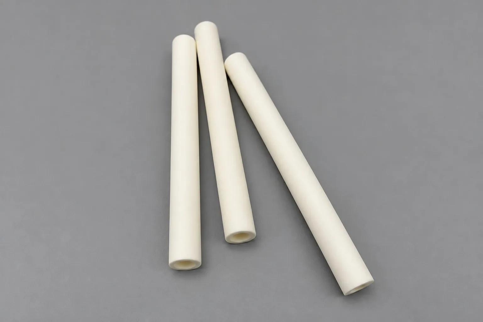 Three white alumina blocks on a grey studio ground, each carrying two raised bosses with bores.