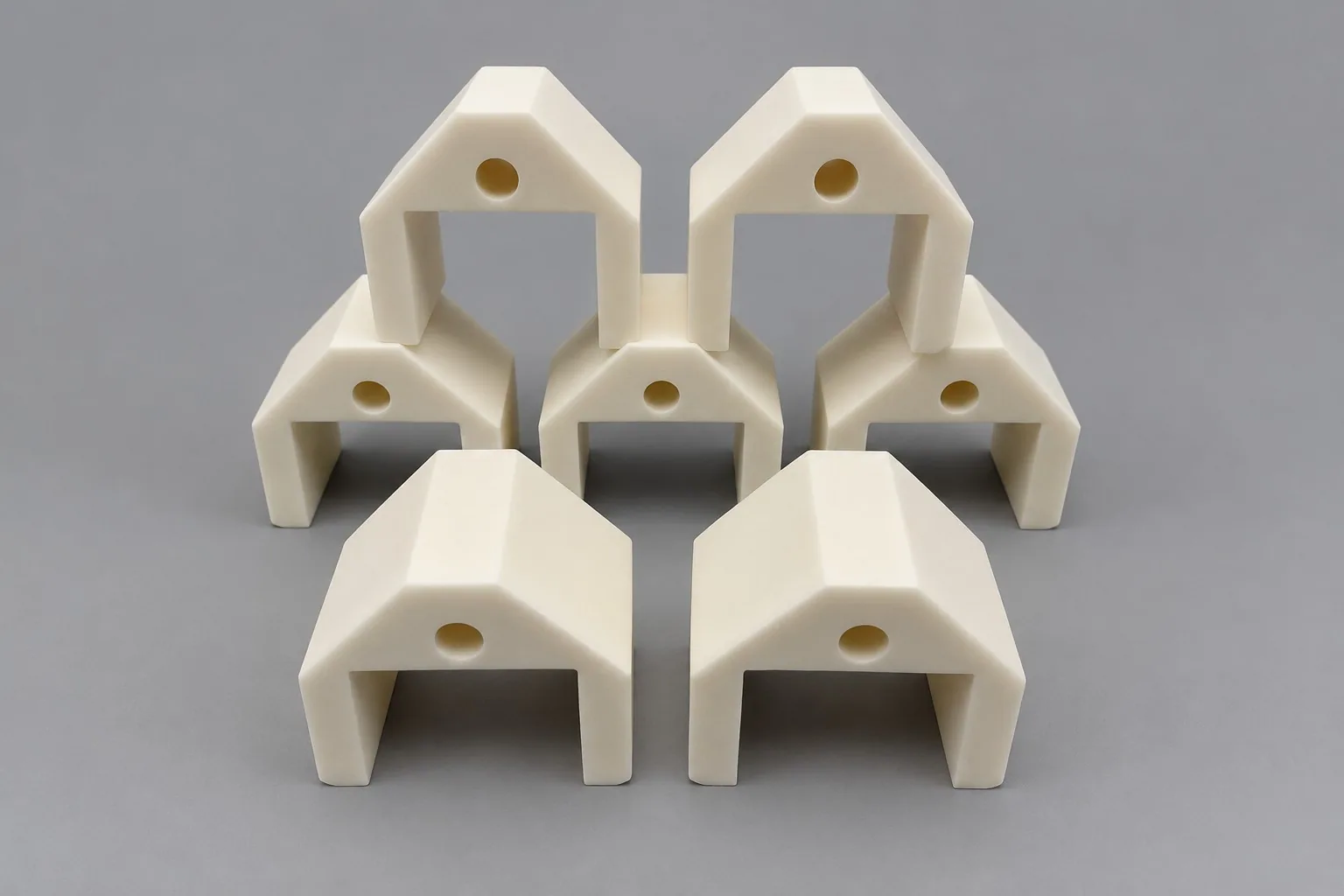White alumina arch-shaped blocks with a bore through the crown, arranged in three rows on a grey studio ground.