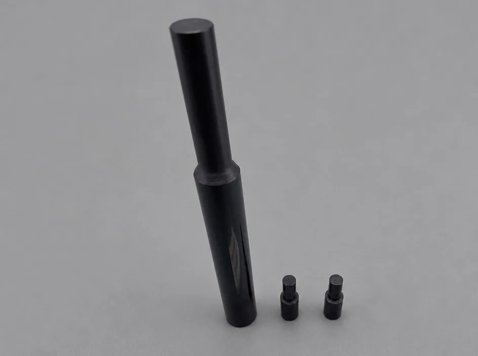 A long black tapered part on a light ground, with two small threaded metal inserts set into a flat near the base.