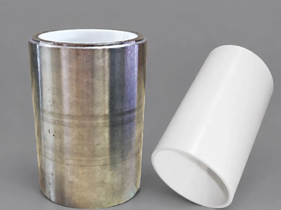 A metal cylinder on a grey studio ground with a white ceramic liner visible inside, beside a second white liner lying at an angle.