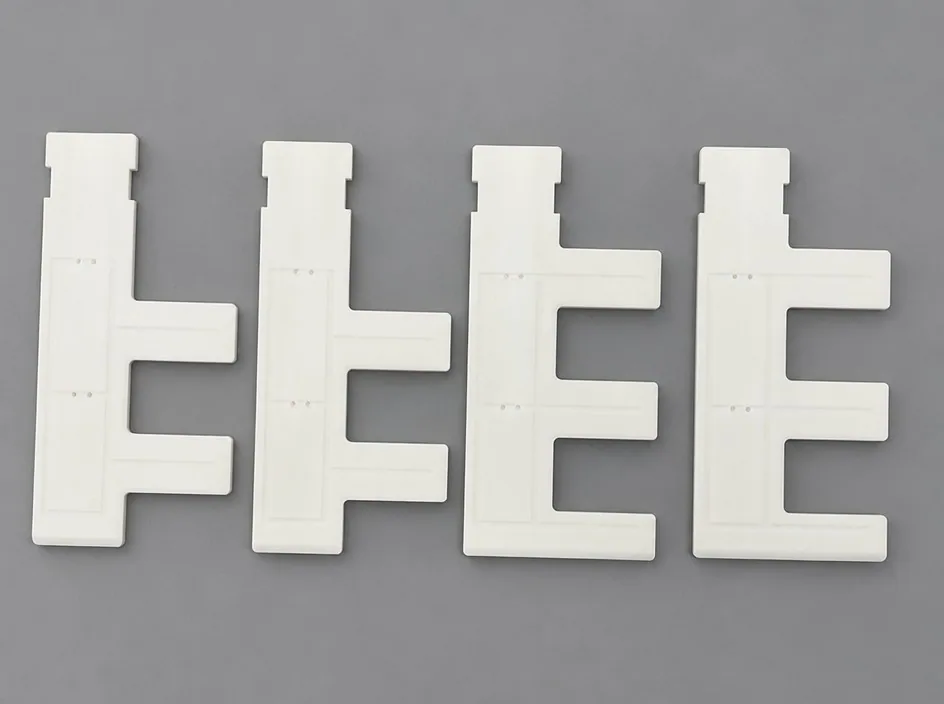 Four white plates on a grey studio ground, each cut to an E-shaped profile with a stepped top edge and projecting teeth.