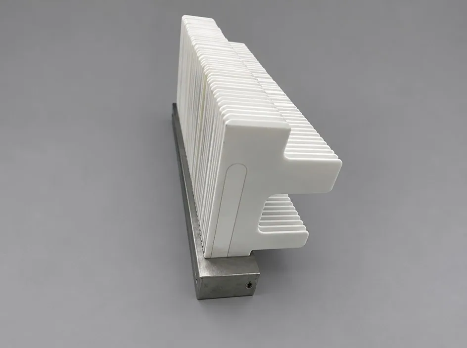A stack of thin white plates held in a machined metal base on a grey studio ground, seen from one end so the laminations read as a ribbed block.
