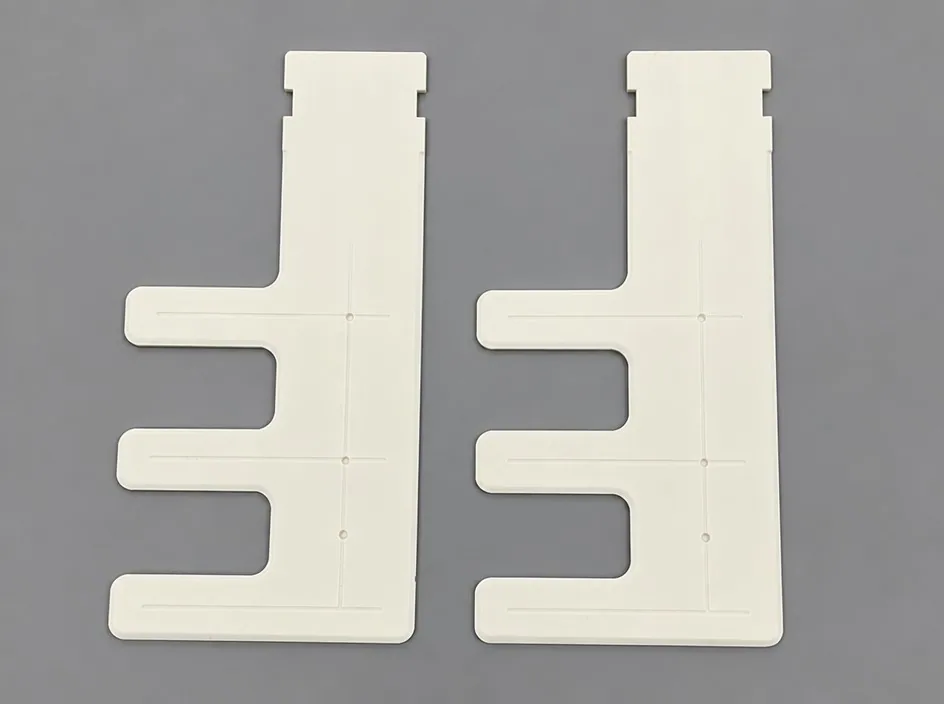 Two white plates on a grey studio ground, each cut to an E-shaped profile with a stepped top edge and three projecting teeth.