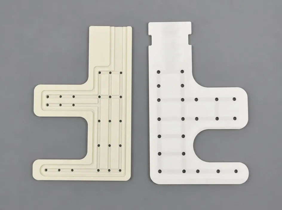 Two white plates on a grey studio ground, both cut to an E-shaped profile and drilled with a grid of small bores.