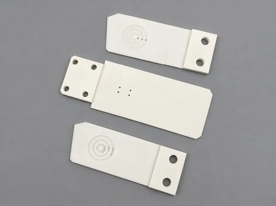 Three white plates on a grey studio ground, each carrying a shallow concentric circular recess and a pair of small bores.
