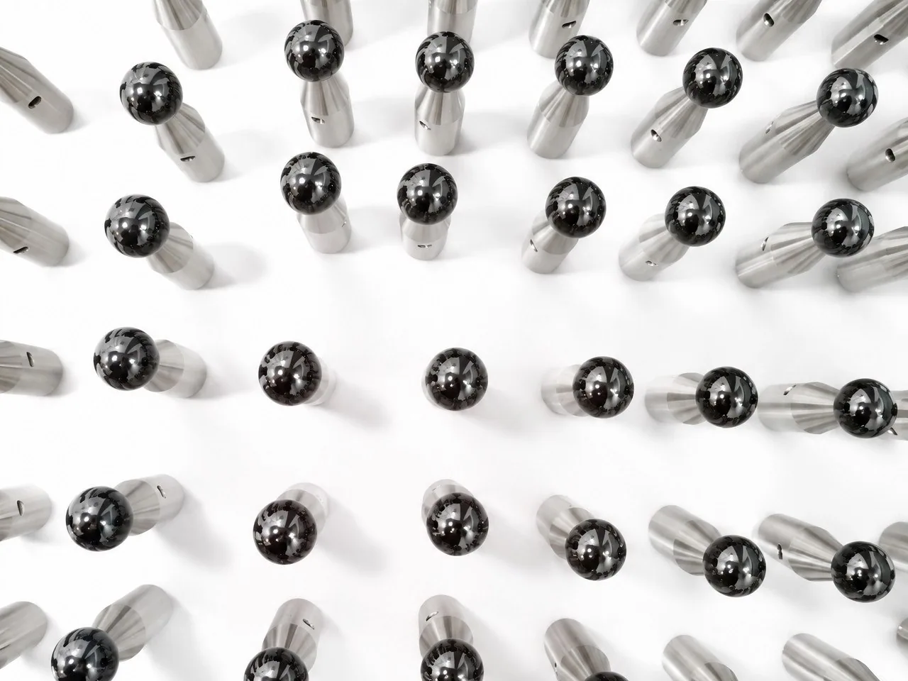 A large batch of ball-tip probes arranged in rows on a white ground, each with a silicon nitride ball on a machined shaft.