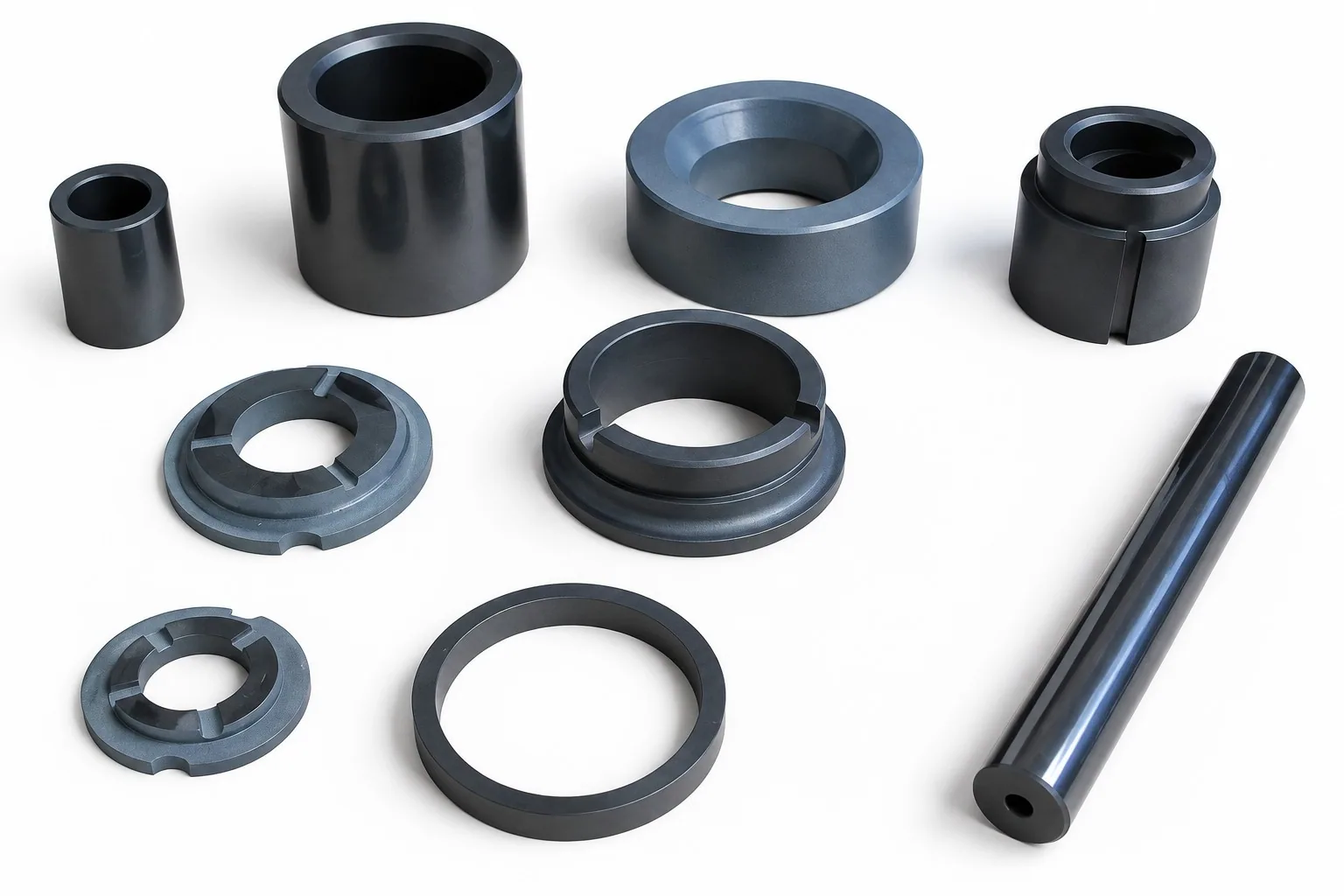 A spread of black silicon carbide parts on a white ground: plain sleeves, slotted rings, discs with lugs and a long rod drilled with a cross hole.