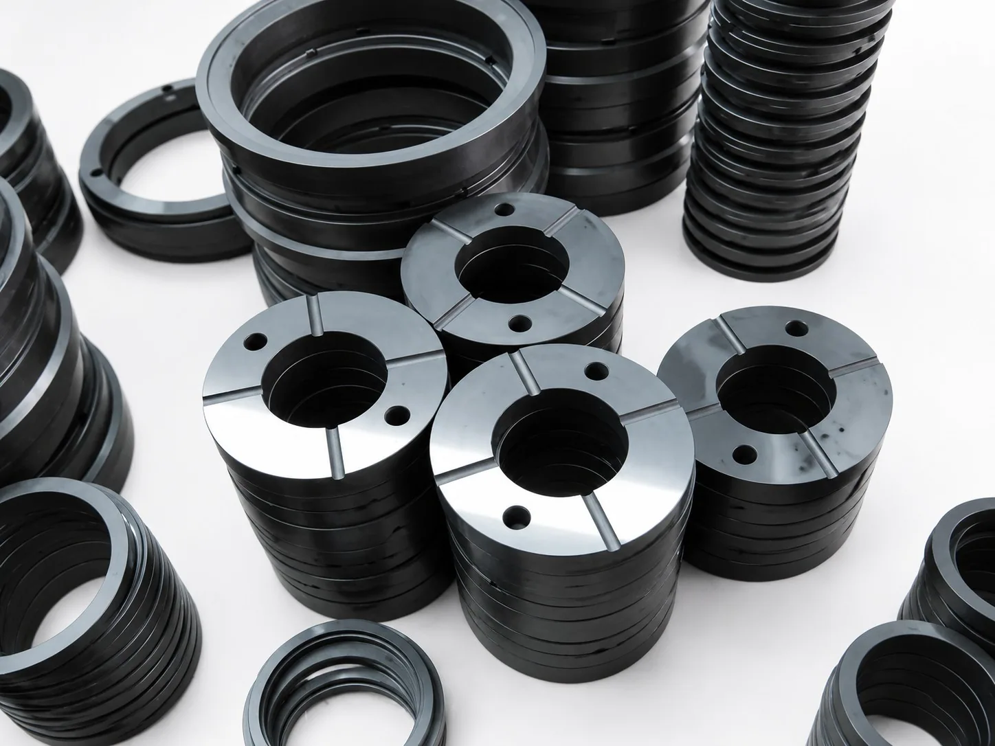 Stacks of black silicon carbide seal rings on a white ground, the top rings drilled with holes and cut with radial slots.