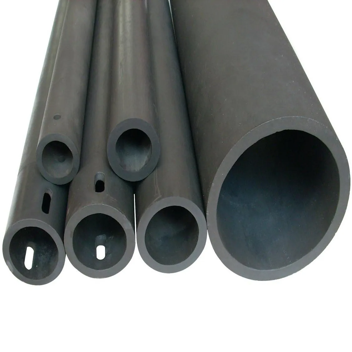 Five long black silicon carbide tubes on a white ground in a range of diameters, several pierced with small holes through the wall.