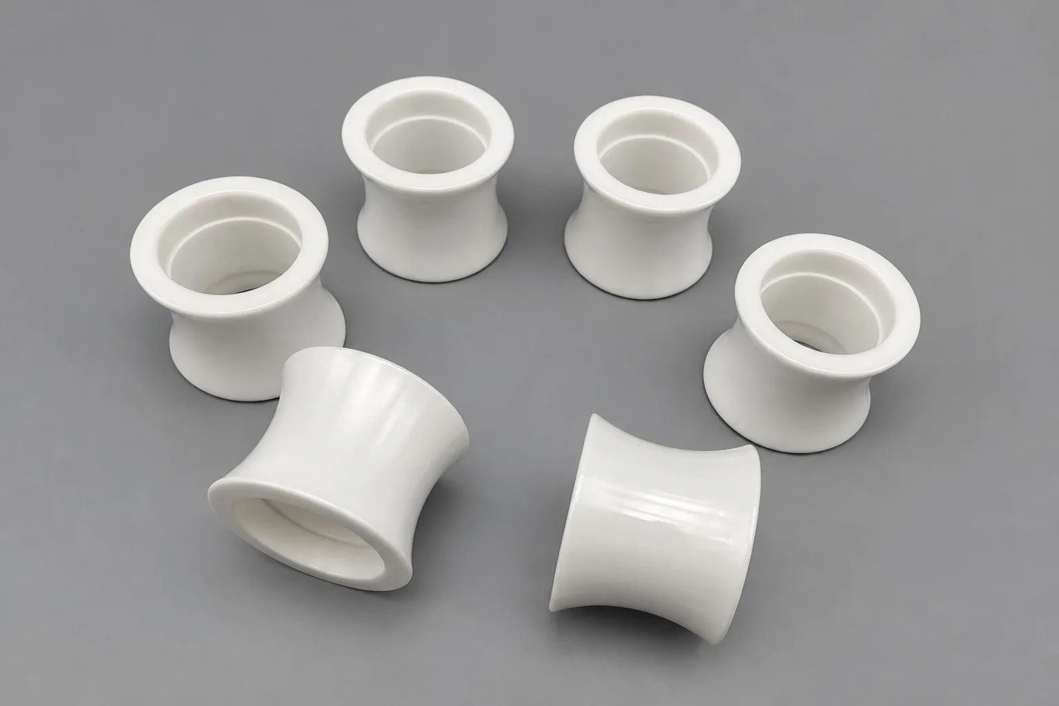 Six white zirconia bushings on a grey studio ground, each a short tube with a flared opening at both ends.