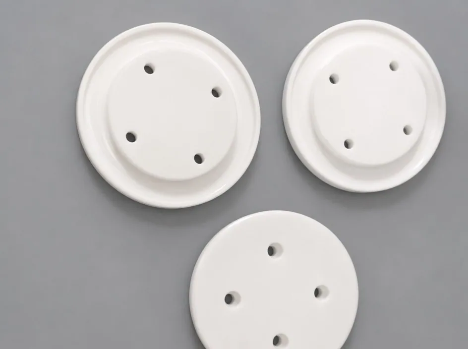 Three round zirconia discs on a grey studio ground, each with a raised rim and four holes through the face.