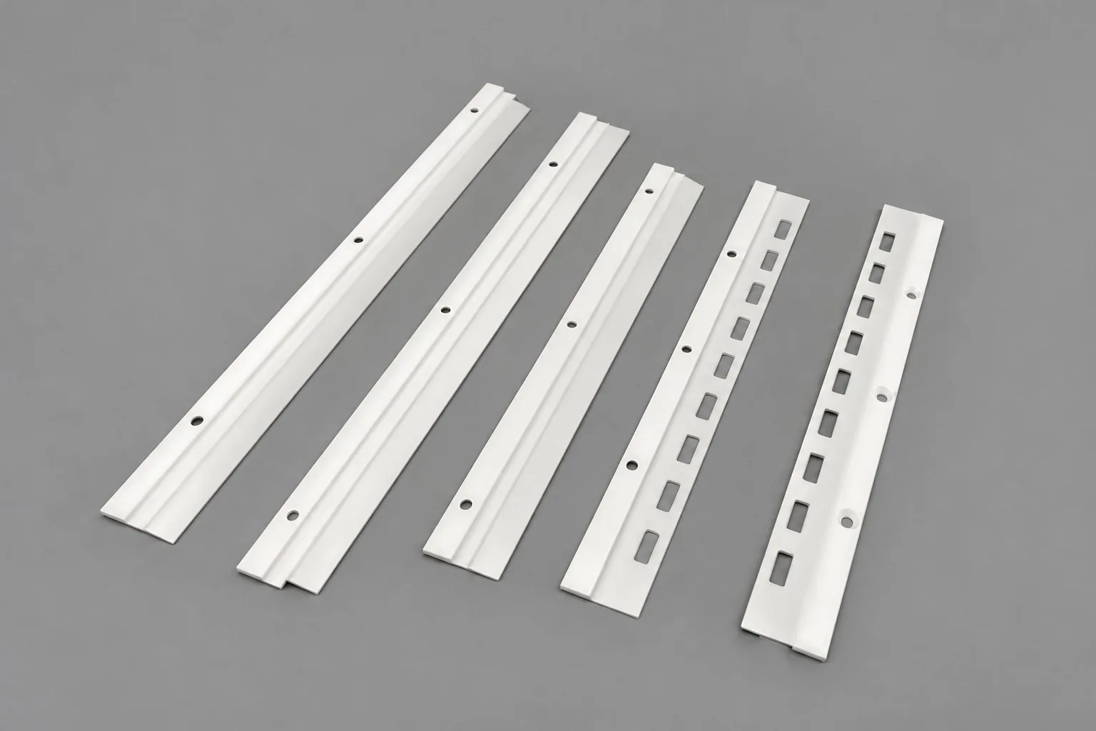 Five zirconia strips on a grey studio ground, carrying drilled holes and, on two of them, rows of elongated slots.