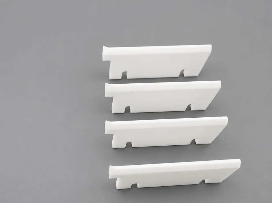 Four zirconia rails on a grey studio ground, each with a raised lip along one edge and two feet cut into the opposite edge.
