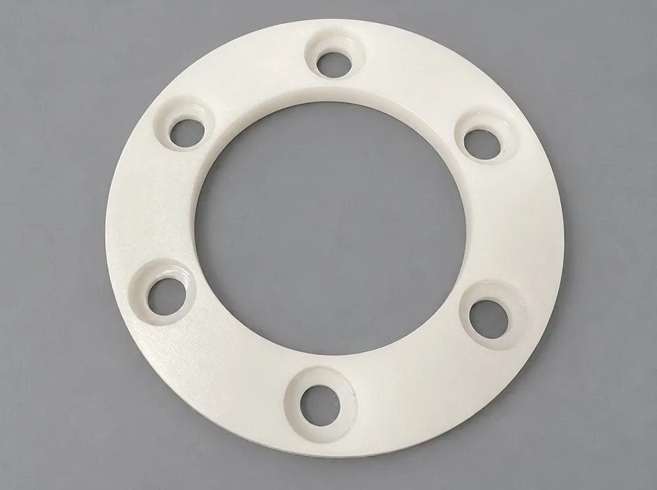 A zirconia annulus on a grey studio ground with six counterbored bolt holes around the rim.
