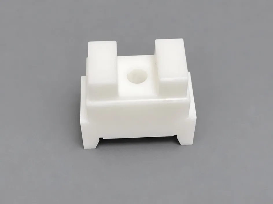 A white zirconia block on a grey studio ground with two raised rails along the top and a central through bore, standing on short feet.