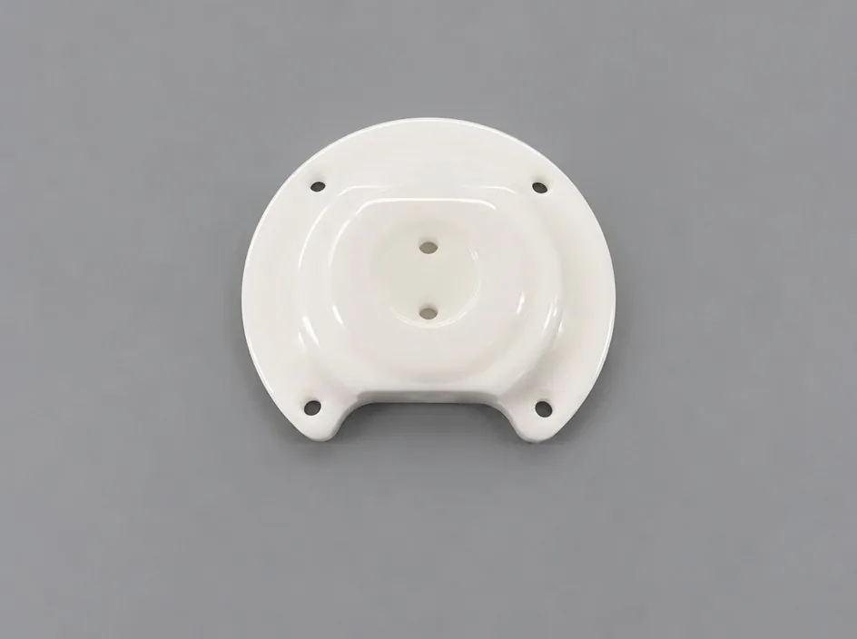 A rounded zirconia plate on a grey studio ground with a raised central boss, two holes through the boss, four mounting holes and a notch in the lower edge.