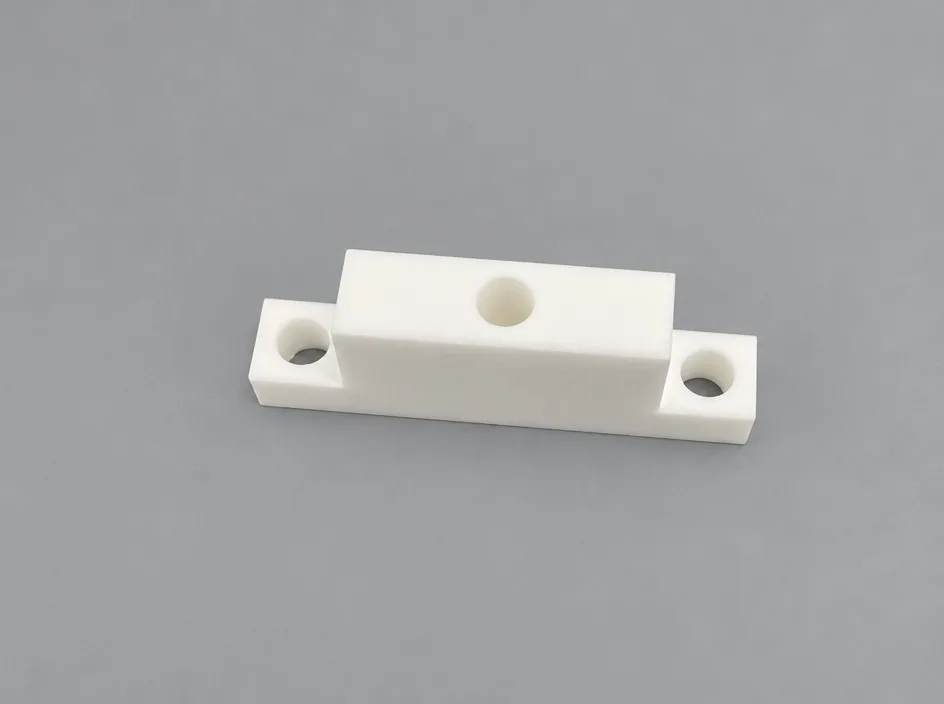 A zirconia block on a grey studio ground with a raised central section and three bores, two at the ends and one in the middle.