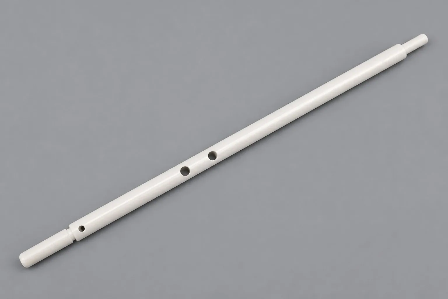 A long zirconia tube on a grey studio ground, stepped down at both ends and drilled with a pair of cross holes near the middle.